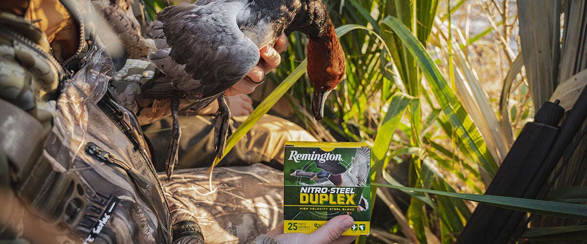 Box of Nitro-Steel Duplex in a field with man holding duck